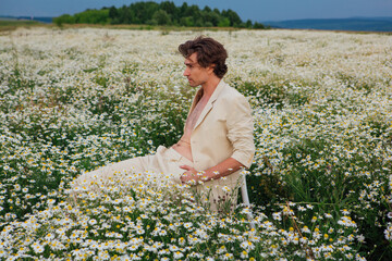 Tall handsome man sitting on a white chair in camomile flowers field