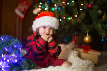 Fototapeta na wymiar a child in red clothes is sitting waiting for the new year. the concept of celebrating Christmas at midnight. holiday costume