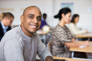 Portrait of focused young adult male studying in classroom with colleagues - obrazy, fototapety, plakaty
