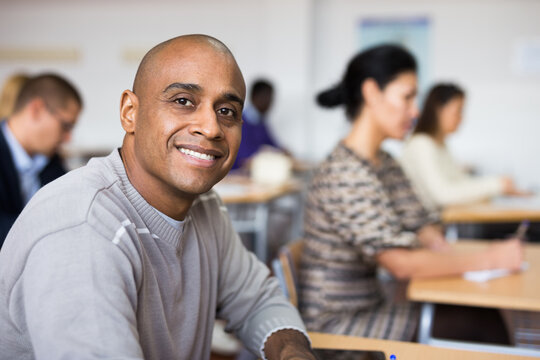 Portrait of focused young adult male studying in classroom with colleagues