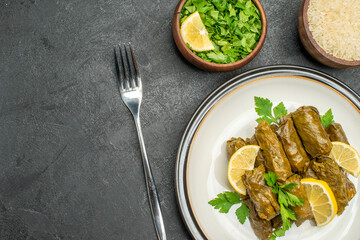 top close view stuffed grape leaves on white plate bowls of parsley and rice a fork on dark background with free space