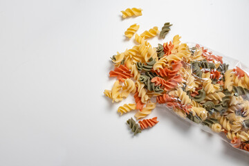 Tricolor Italian Fusilli pasta package opened with noodles spilling out of the package on a white surface. Concept foods rich in carbohydrates.