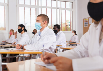 Focused man studying in classroom with colleagues medicals in protective face masks for disease prevention during training program for health workers