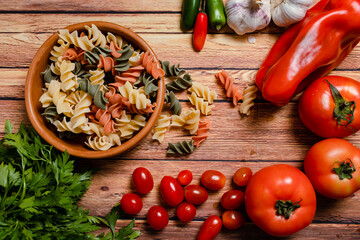 Terracotta bowl with tricolor fusilli noodles and cherry and round tomato, chili peppers, garlic and parsley. Food raw material concept. Chopped angle.