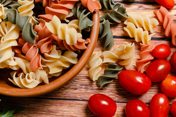 Terracotta bowl with tricolor fusilli noodles and cherry and round tomato, chili peppers, garlic...