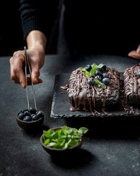 Pastry chef decorates brownie cake with blueberries and mint leaves