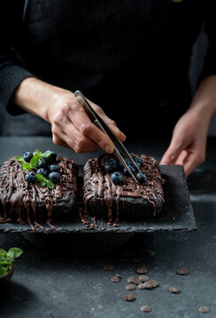 Pastry chef decorates brownie cake with blueberries and mint leaves