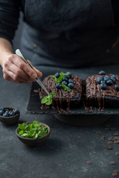 Pastry chef decorates brownie cake with blueberries and mint leaves
