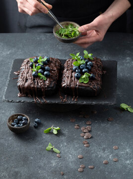 Pastry chef decorates brownie cake with blueberries and mint leaves