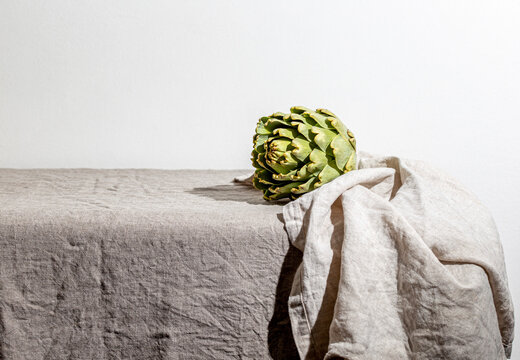 Artichoke on the table covered with a gray linen tablecloth.
