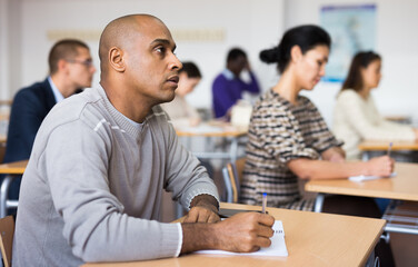 Young positive man listening to lecture taking notes at adult education class