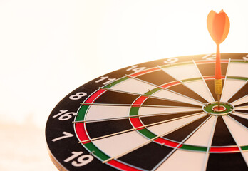 Fototapeta premium Dart arrow hit to center on bullseye(bull's-eye) of a dartboard is a target of purpose challenge business at sunset, expert strategy market target, objective financial and goal a concept
