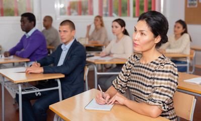 Young positive woman sitting at desk in classroom working during lesson at adult education class