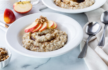 A bowl of steel cut oats with brown sugar garnished with apple slices and walnuts.