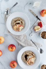 Top down view of bowls of steel cut oats and brown sugar garnished with apples and walnuts.