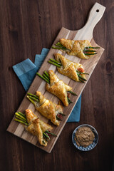 Asparagus and prosciutto puff pastry bundles on a wooden cutting board with grainy dijon mustard for dipping.