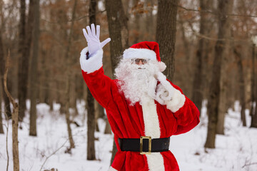 Walking through the winter forest, Santa Claus waves his hand carrying Christmas presents