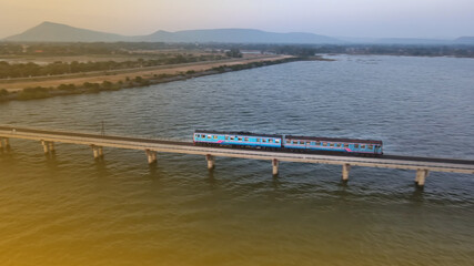 Fototapeta na wymiar Aerial view of Thailand passengers train running on the floating railway bridge during sunset in the lake of 