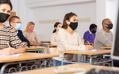Young woman in protective face mask listening to lesson in extension school. Concept of necessary...