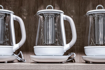 Electric white kettles. Stand in a row. On a brown background. View from the front.