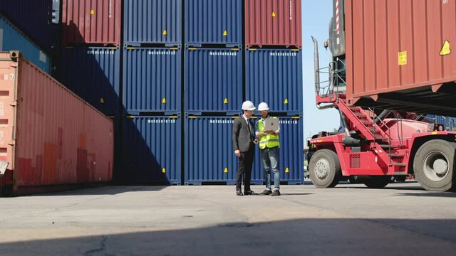 Wide shot of Asian engineer discuss and work with Caucasian cargo container worker or technician and stand in front of big brown container. Concept of good teamwork support delivery and logistics.