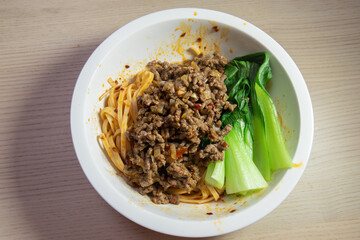 A bowl of spicy noodle with minced meat and bok choy.