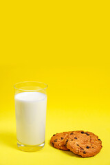 Chocolate chip cookies and a glass of milk on a bright yellow background.