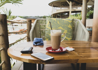 Hot coffee latte in glass with phone and wallet on wooden table outdoor terrace of cafe.