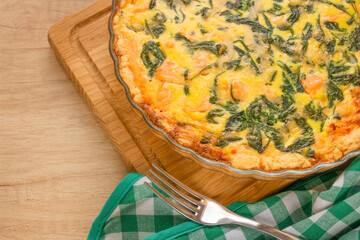 Close up of salmon fish and baby spinach leaves quiche pie - homemade recipe pie on wooden table background with copy space, selective focus