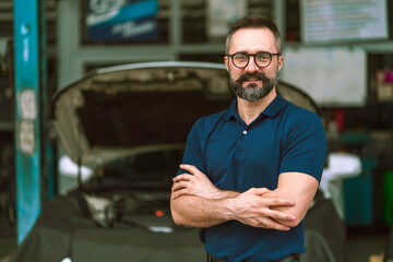 Portrait of professional auto mechanic standing in front of the garage 