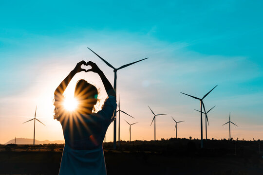 Wind turbines farm is an alternative electricity source, Concept of sustainable resources, Renewable energy concept, Girl standing and watching the sunset with wind generators turbines to backgrounds