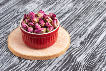 Dried damask rose buds in small red bowl on wooden table.