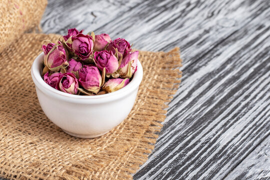 Dried damask rose buds in small white bowl on black wooden table.
