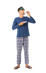 Portrait of young man with sleep mask drinking coffee on white background