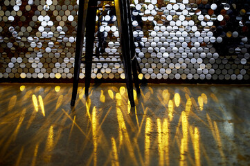 High stool on a metal base against the background of the wall with sequins. The glare is reflected on the floor. Glamorous design