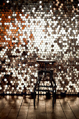 High stool on a metal base against the background of the wall with sequins. The glare is reflected...