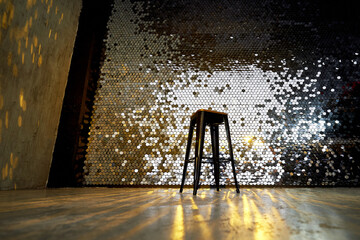 High stool on a metal base against the background of the wall with sequins. The glare is reflected...