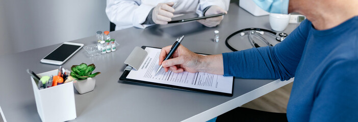 Senior woman filling in consent form for coronavirus vaccine with her doctor