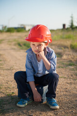 Naklejka na ściany i meble upset little kid in orange helmet sitting on road to factory industrial plant being fired