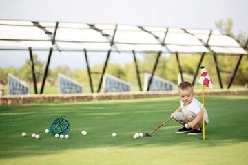 Little boy golfer with his plastic golf set on green field outdoor, collecting his golf balls