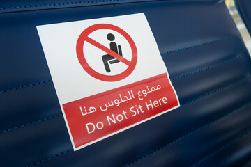 Sticker sign 'Do not sit here' in english and arabic on a seat at the airport, travel during coronavirus pandemic, social distancing in the terminal.