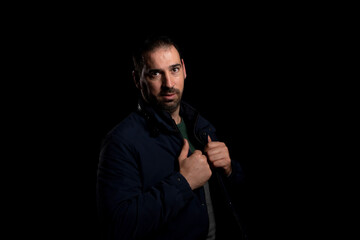 Bearded man holding the lapels of his blue jacket posing isolated on black background