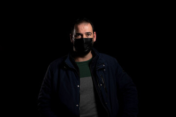 Bearded man equipped with a mask to protect himself from coronavirus wearing a blue jacket posing isolated on black background