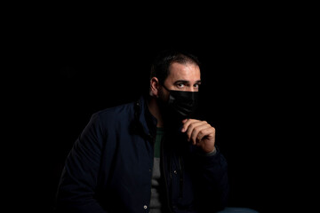 Bearded man equipped with a mask to protect himself from coronavirus wearing a blue jacket posing isolated on black background