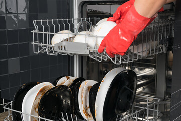 hands in red rubber gloves load dirty dishes into the dishwasher