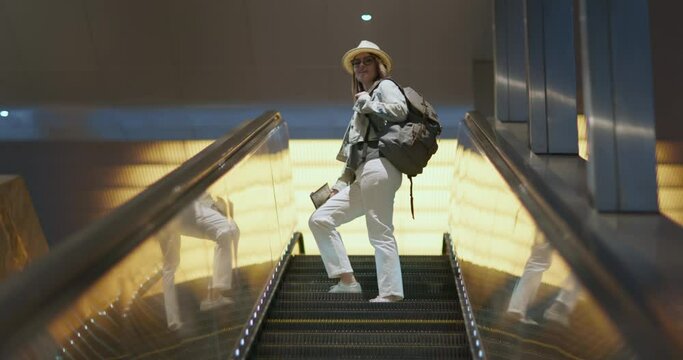 Stylish plus size model and happy people slow motion 4K footage. Smart smiling woman in glasses with backpack going up on escalator in the shopping mall, airport, or subway, metro station in the city