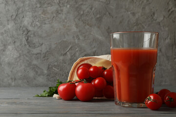 Glass of tomato juice and tomatoes on gray wooden table