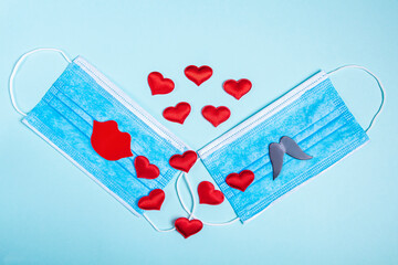 Valentine's day composition. Two medical face protective mask with paper lips and mustache and red hearts on blue background. New normal and coronavirus pandemic, COVID-19 concept. Copy space for text