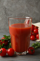 Glass of tomato juice and tomatoes on gray wooden table