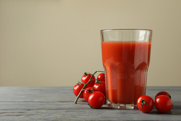 Glass of tomato juice and tomatoes on gray wooden table